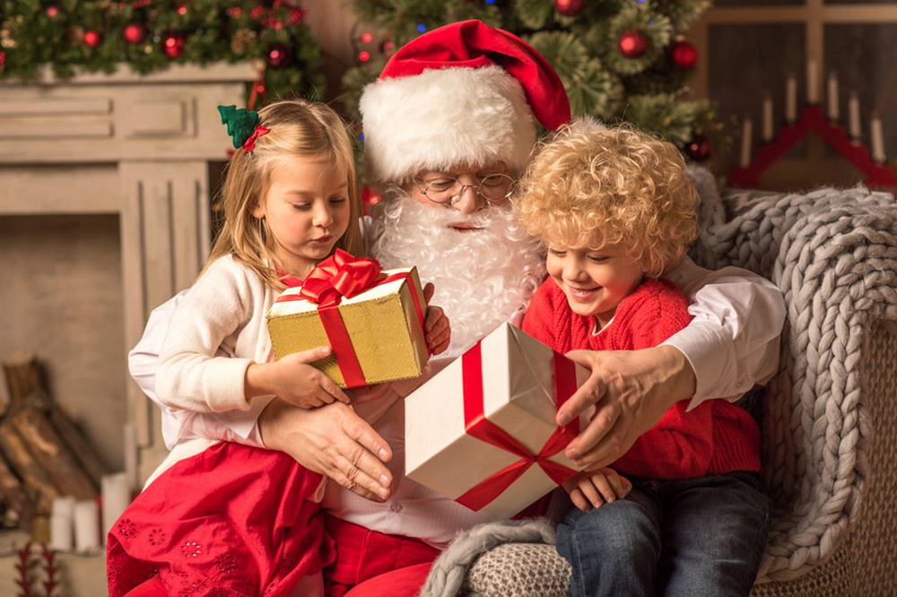 Santa gives gifts to children in cozy Christmas scene with festive decorations.