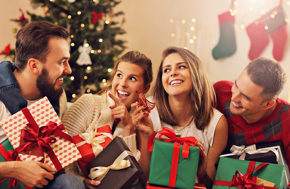 Celebrating Christmas with friends: joyful gift exchange in front of decorated tree.