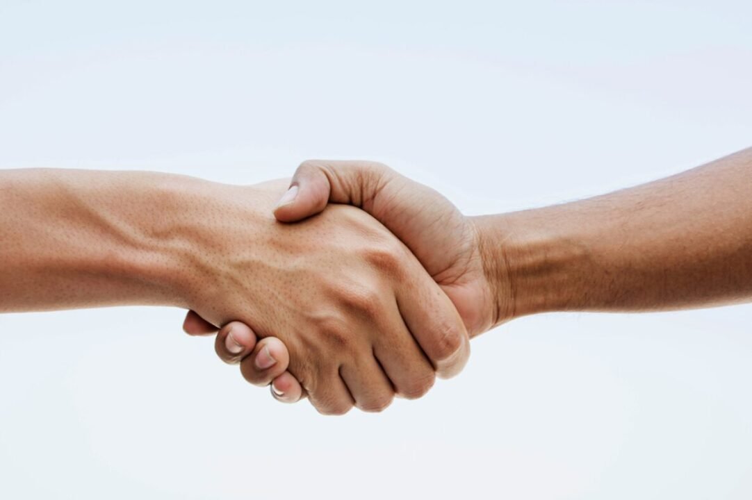 Close-up of two hands, one with a lighter skin tone and one with a darker skin tone, engaged in a firm handshake against a white background.