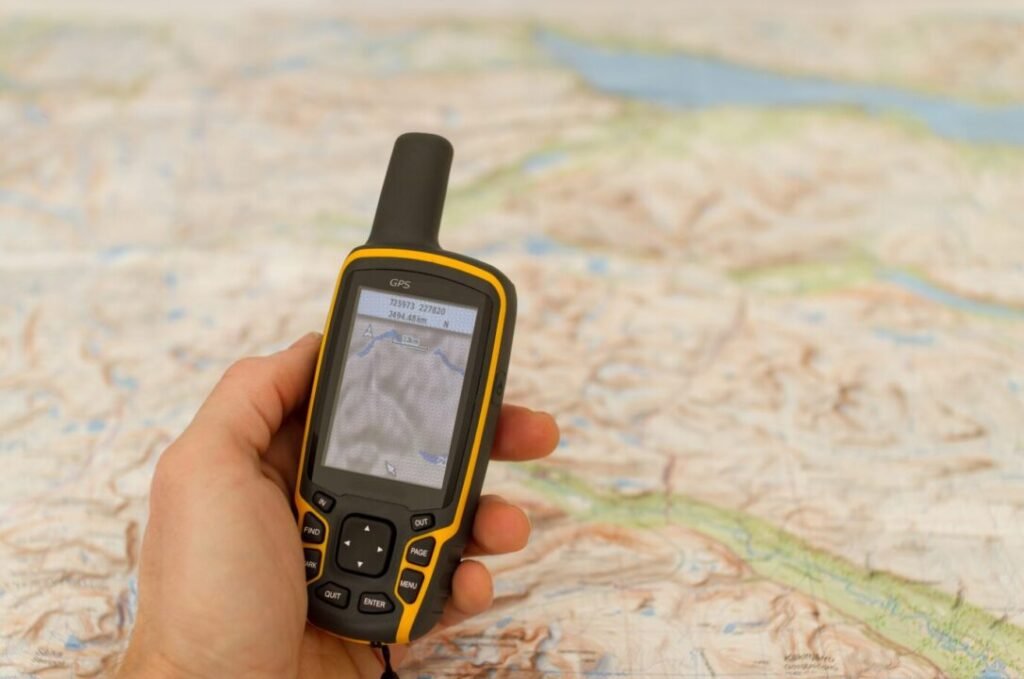 Hand holding a yellow and black GPS device over a topographic map.