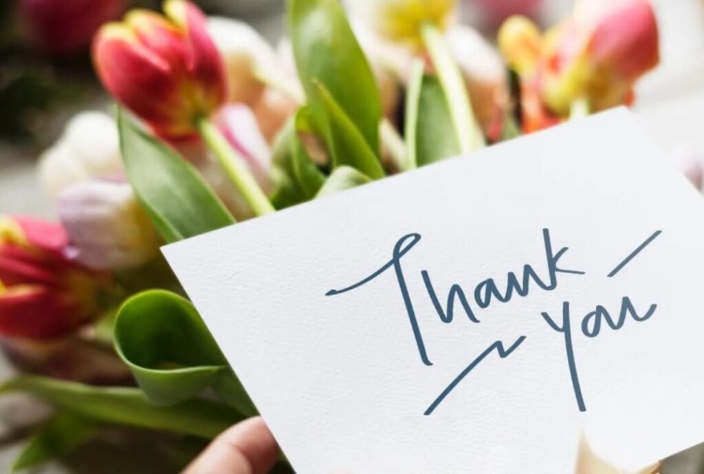 Close-up of a hand holding a "Thank you" card with colorful tulips in the background.