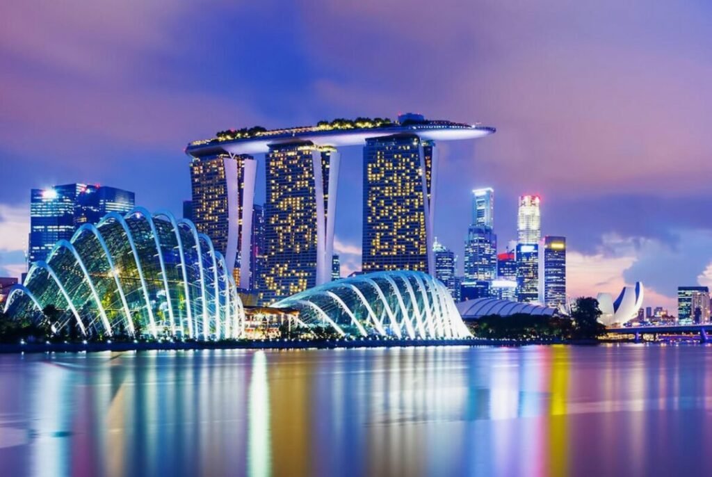 Nighttime view of Marina Bay Sands, Cloud Forest Domes, and Singapore skyline reflected in the water.