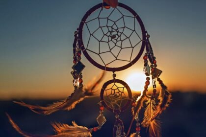 Dreamcatcher with feathers and beads held against a sunset sky.