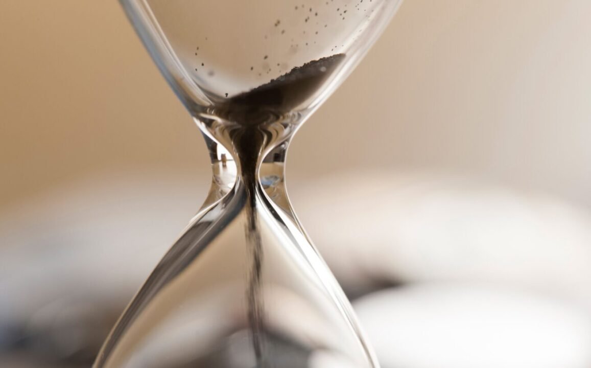 Close-up of an hourglass with sand flowing through the narrow middle.