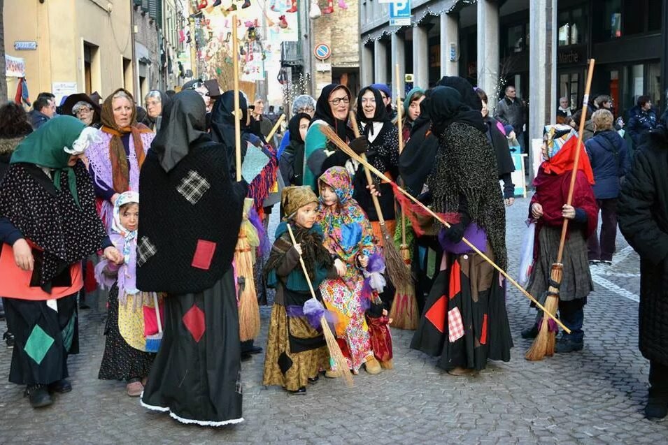 People dressed in colorful costumes and holding brooms gather on a cobblestone street during a festive event.