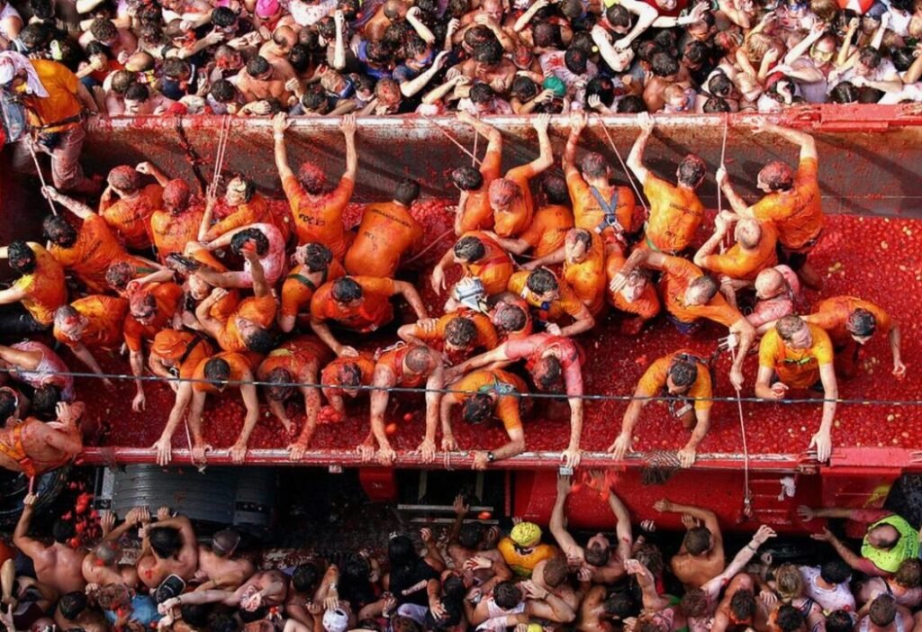 People crowded in and around a truck filled with tomatoes, participating in a tomato-throwing festival.
