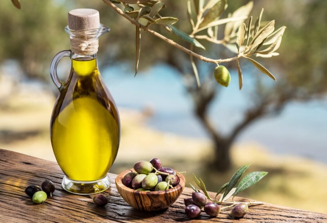 Rustic Mediterranean still life with olive oil, olives, and olive branches on wooden table.