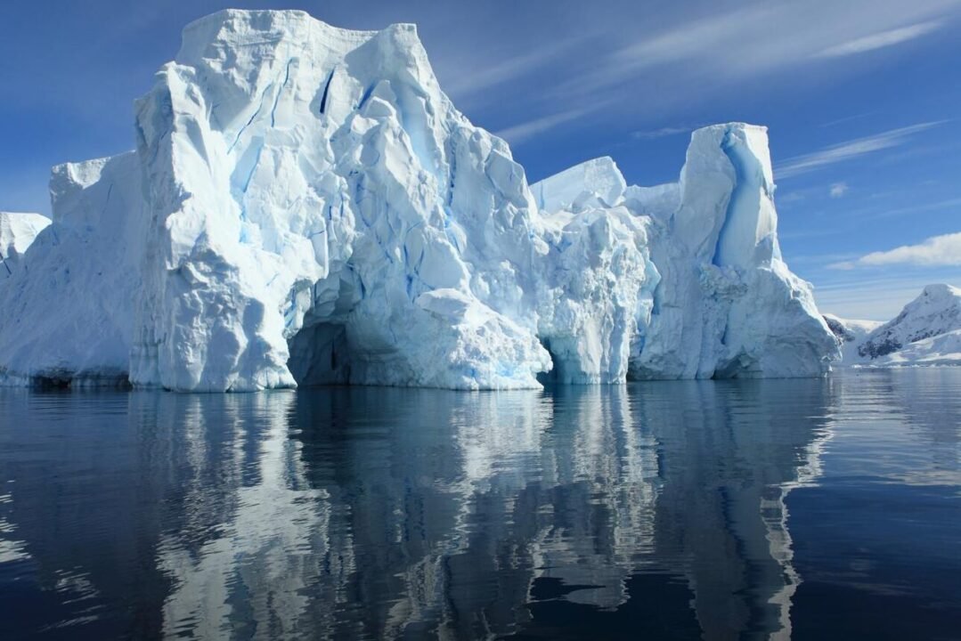 Massive icebergs with blue and white hues reflected in a calm sea under clear skies.