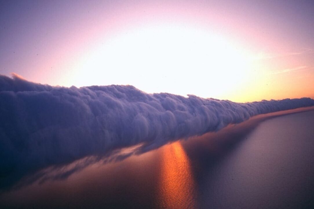 Surreal sunset sky with cloud wave reflected on calm water, creating serene natural beauty.
