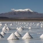 Majestic salt cones on a reflective flat with snow-capped mountains in the background.