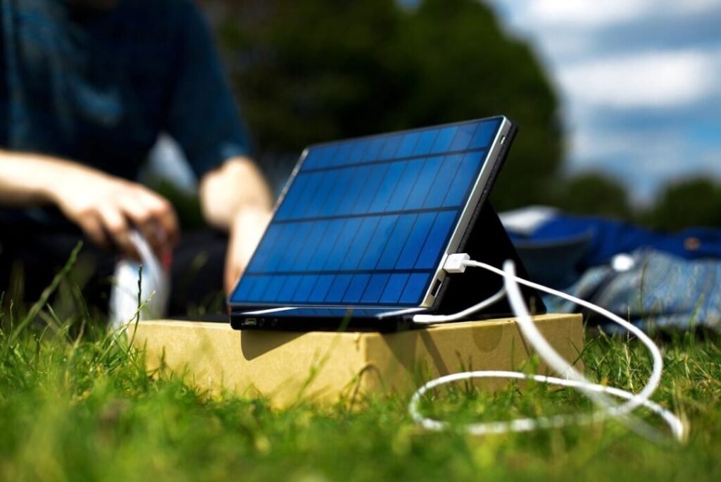 A portable solar panel placed on the grass, connected to a device with a USB cable, with a person in the background.