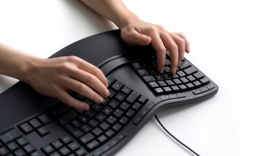 Person typing on an ergonomic split keyboard on a white desk.