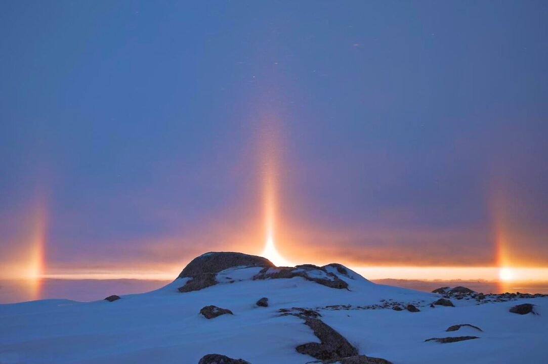 Winter light pillars shining over snow-covered landscape at twilight, creating a stunning natural spectacle.