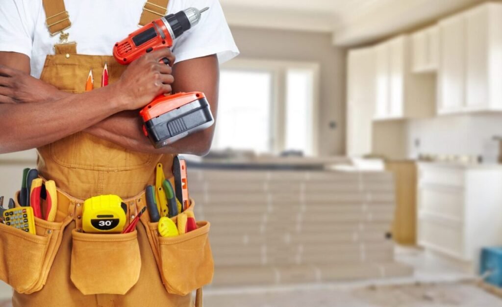 Construction worker in a tool belt holding a cordless drill, standing in a modern kitchen under renovation.