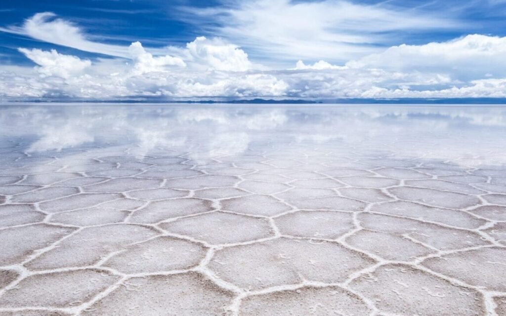 Vast salt flats reflecting the sky with pentagonal and hexagonal patterns on the ground and scattered clouds above.