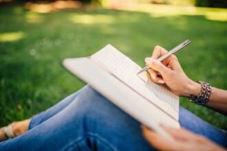 Person writing in a notebook while sitting on grass.