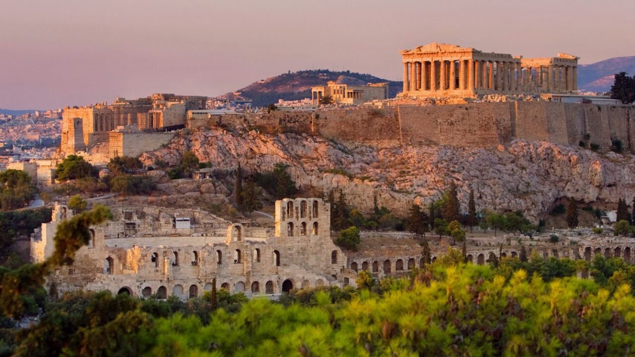 View of the Acropolis in Athens, Greece, featuring the Parthenon illuminated by sunset.