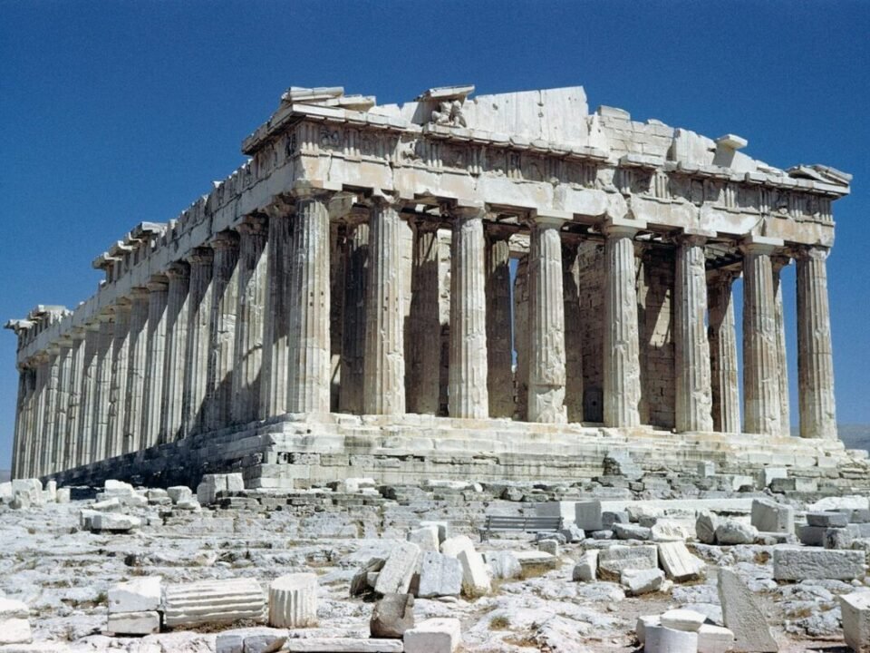 The Parthenon, an ancient Greek temple with Doric columns, partially ruined, set against a clear blue sky.