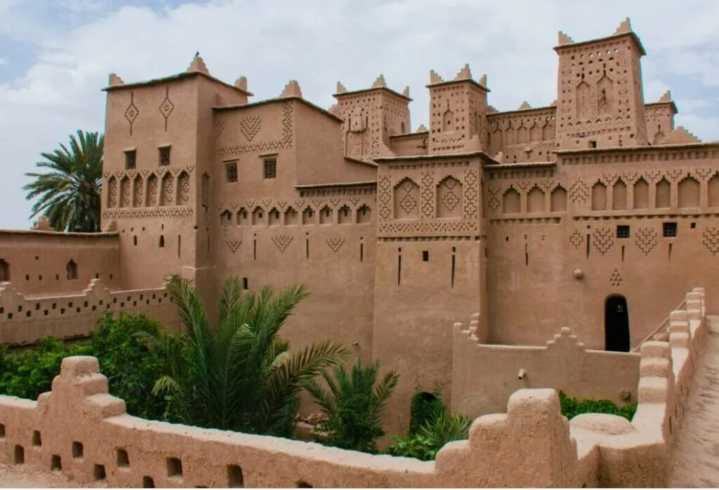 Traditional mud-brick kasbah with decorative patterns and palm trees in the foreground.