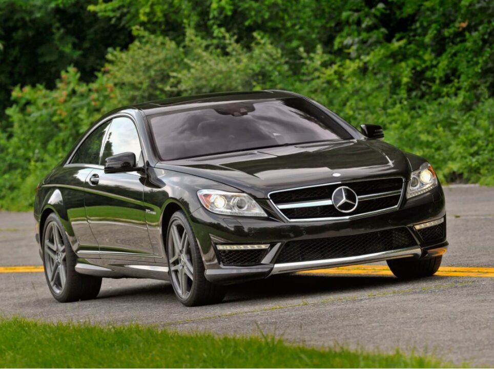 Black Mercedes-Benz coupe driving on a road with green foliage in the background.