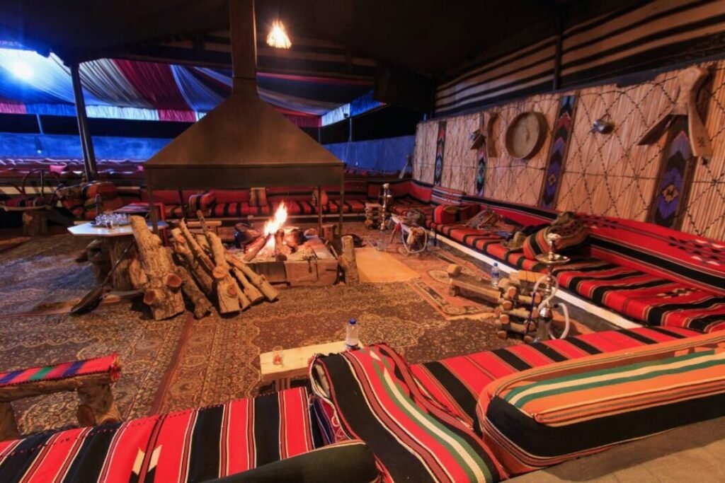 A traditional Bedouin tent with colorful cushions and rugs, centered around a fire pit with a chimney.