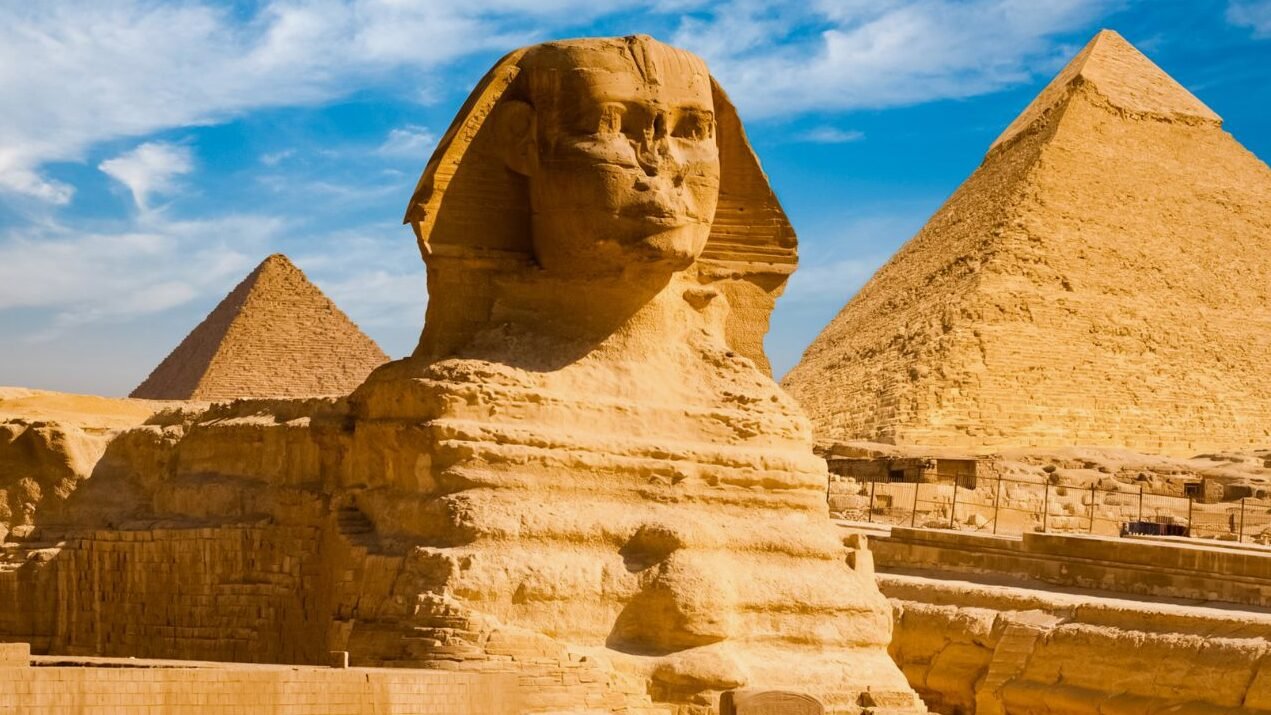The Great Sphinx of Giza with pyramids in the background on a sunny day.