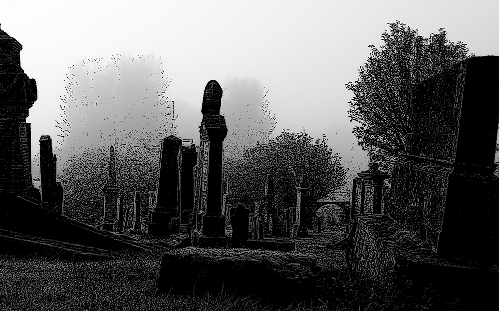 Foggy cemetery with tall, dark gravestones and trees in the background.