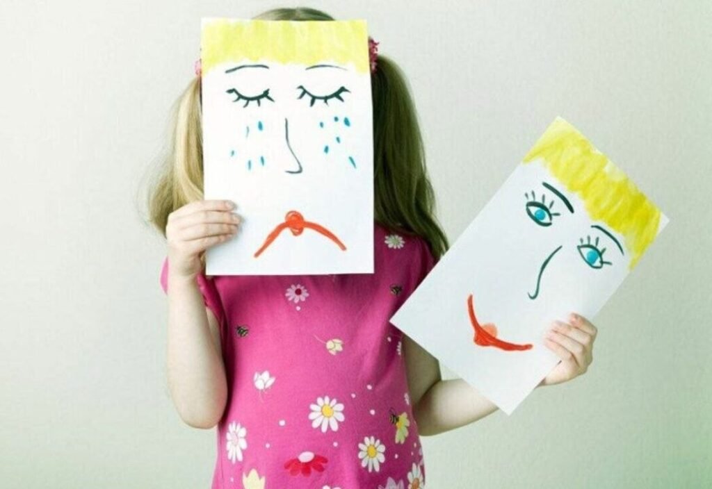 Child holding two drawings of faces, one sad and one happy.