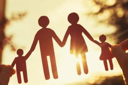 Silhouette of a paper cutout family holding hands against a sunlit background.