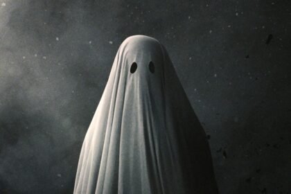 Person dressed as a ghost, covered in a white sheet with two black eye holes, standing against a dark, speckled background.