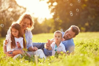 A family sitting on grass in a park, blowing bubbles and smiling.