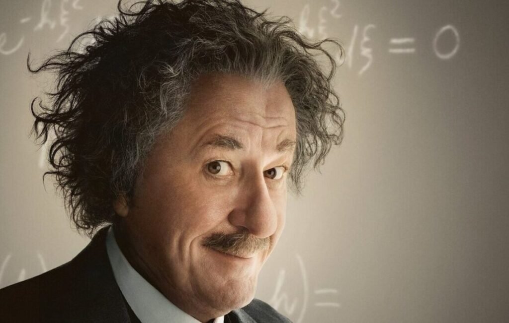 A smart person with wild, curly hair and a mustache, smiling slightly, against a background with mathematical equations.