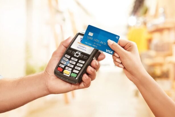 A hand holding a blue contactless Visa card near a card reader for payment.