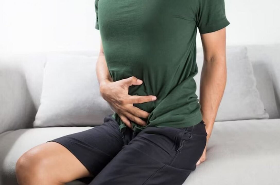 A person sitting on a couch, holding their stomach in discomfort.