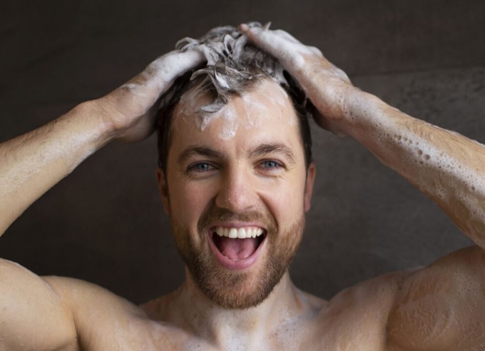 A man smiling while washing his hair with shampoo, creating a lather.